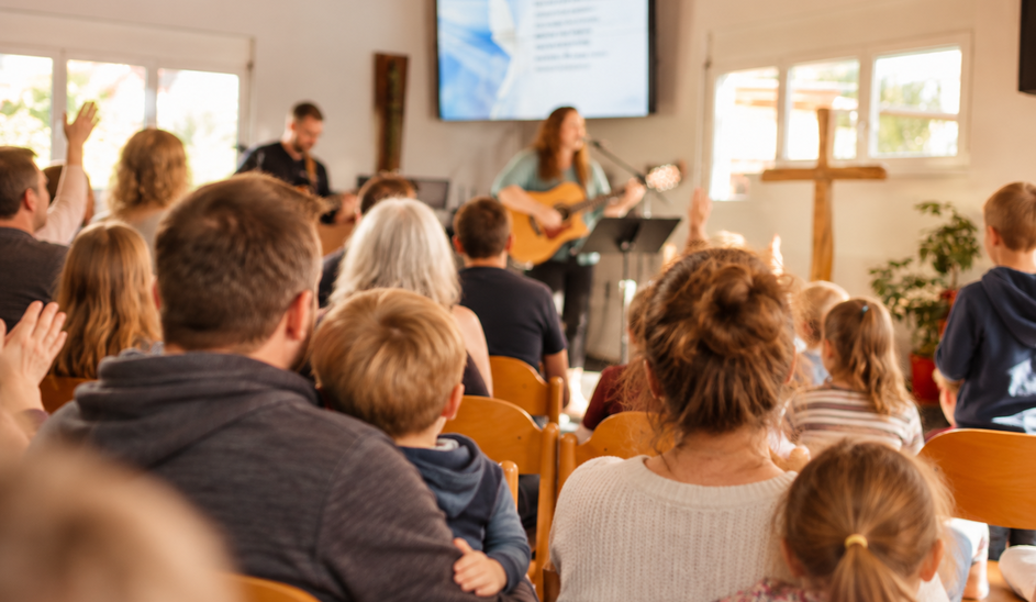 Symbolbild (KI-generiert): Familien mit Kindern nehmen gemeinsam an einem Gottesdienst teil. Im Hintergrund gestaltet eine Musikgruppe den Lobpreis.